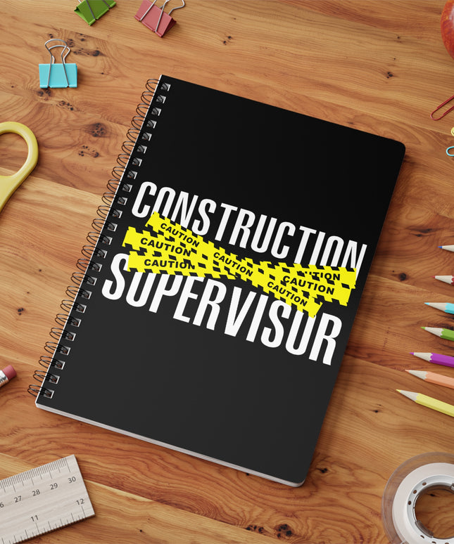 Notebook with 'Construction Supervisor' text on a wooden surface with stationery items.