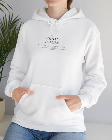 Person wearing a white hoodie with text, standing against a plain background with a plant on the side.