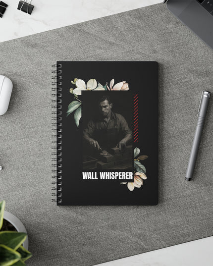 Notebook with 'Wall Whisperer' design on a desk with a pen and airpods.