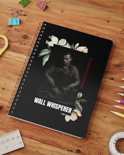 Notebook with 'Wall Whisperer' design on a wooden surface with stationery items.