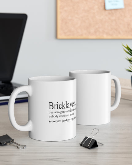 Two white mugs with text on a desk with office supplies and a plant.