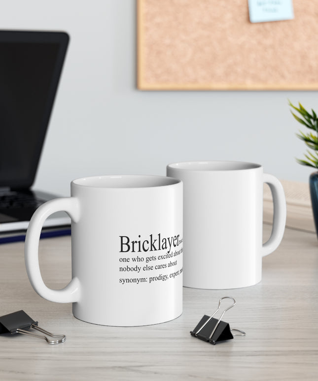 Two white mugs with text on a desk with office supplies and a plant.