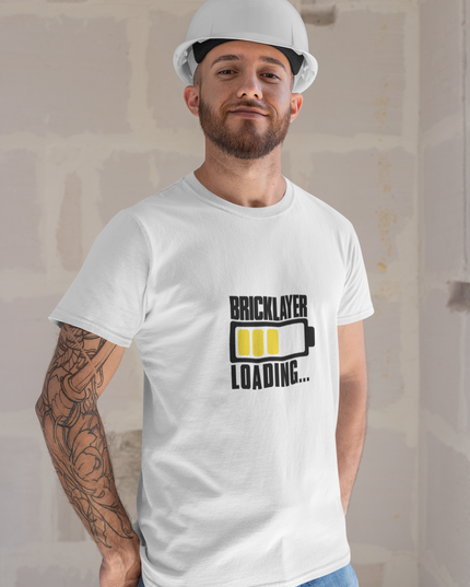 Man wearing a white t-shirt with 'Bricklayer Loading...' graphic and a hard hat indoors.