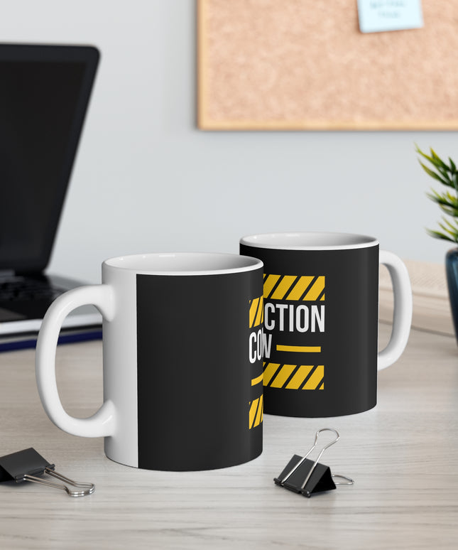 Two black mugs with yellow text "Construction Crew" on a desk with office supplies and a plant.