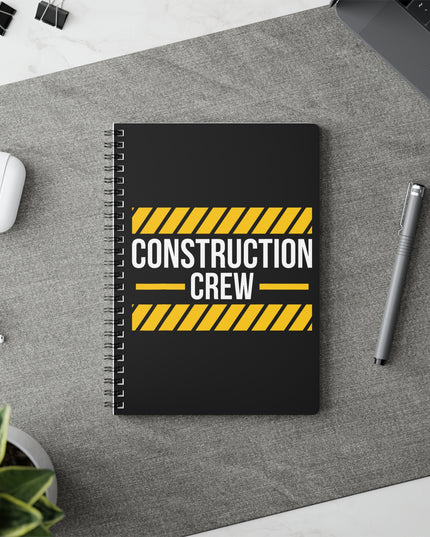 Notebook with 'Construction Crew' design on a desk with a pen and earbuds.