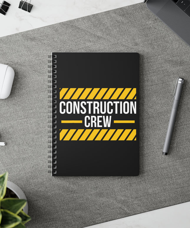 Notebook with 'Construction Crew' design on a desk with a pen and earbuds.