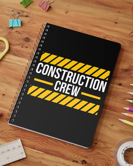 Notebook with 'Construction Crew' design on a wooden surface with stationery items.