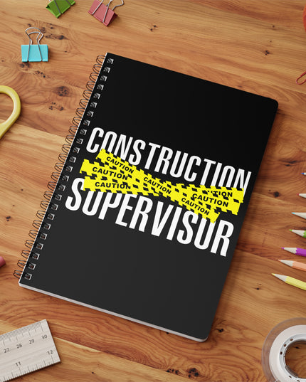 Notebook with 'Construction Supervisor' text on a wooden surface with stationery items.