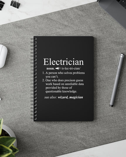 Black notebook with electrician definition on a desk with a pen and earbuds.