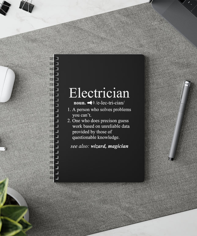 Black notebook with electrician definition on a desk with a pen and earbuds.