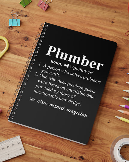 Black notebook with 'Plumber' definition on a wooden surface with stationery items.