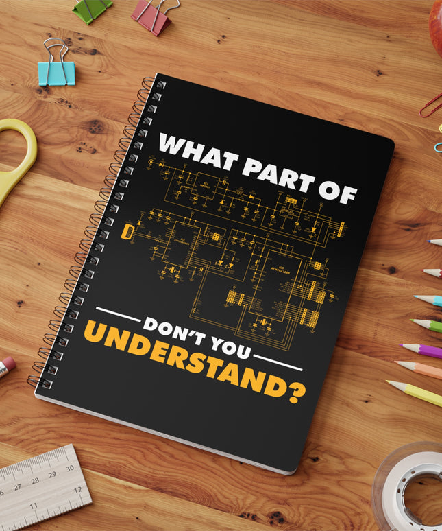 Black spiral notebook with "What part of don't you understand?" graphic, on a wooden table